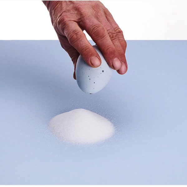 Egg saltshaker by DE INTUITIEFABRIEK. Salt pile on blue tabletop.